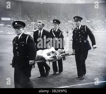 Le footballeur des Blackburn Rovers, Dave Whelan, porté sur une civière par des officiers de l'ambulance St Johns, le manager Dally Duncan tenant sa main. Le joueur s'est cassé la jambe lors de la finale de la FA Cup 1960 contre les Wolverhampton Wanderers à Wembley. Douglas Duncan Banque D'Images