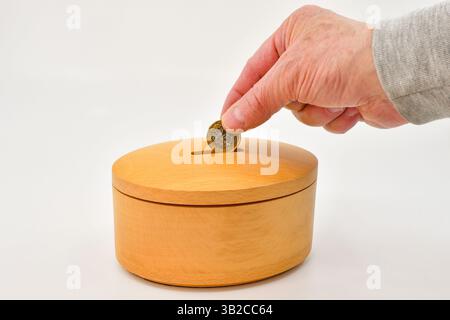 Une pièce de monnaie d'une livre étant mis dans la fente d'une boîte à monnaie en bois. Concept d'enregistrement. Banque D'Images