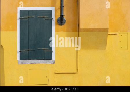 Mur texturé jaune avec volets verts fermés à Burano Italie Banque D'Images