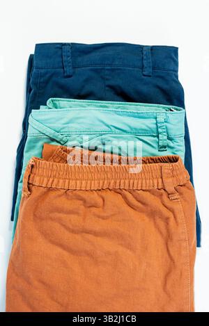 Pantalon décontracté soigneusement plié dans de nombreuses couleurs placé sur une surface de table blanche. Banque D'Images