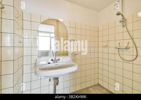 Une salle de bains élégante et minimaliste avec carrelage blanc, un lavabo simple avec un robinet moderne et un miroir ovale. L'espace transmet une ambiance propre et rafraîchissante. Banque D'Images