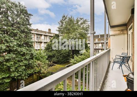 Un balcon urbain serein avec vue sur un jardin luxuriant entouré de bâtiments résidentiels, avec des chaises pour la détente et la tranquillité. Banque D'Images