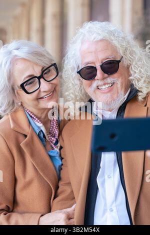 Couple senior caucasien souriant et prenant selfie avec smartphone à l'extérieur Banque D'Images