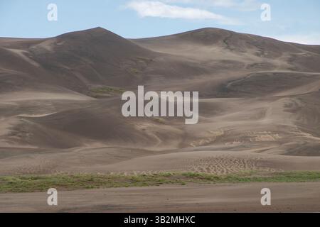 De vastes dunes de sable s'élèvent majestueusement sous un ciel lumineux, mettant en valeur la beauté naturelle. Le soleil projette des ombres sur le terrain vallonné, créant un serein Banque D'Images