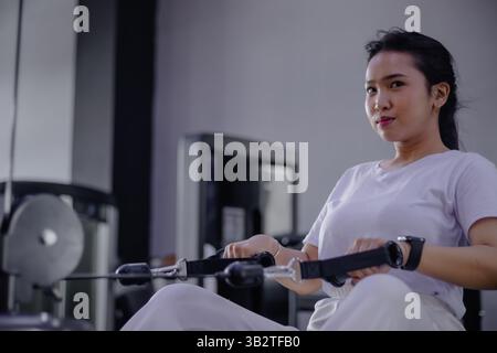 Jeune femme dévouée à la formation de vêtements de sport sur une machine à ramer dans une salle de sport moderne. Concentrez-vous sur la forme physique et un mode de vie sain. Renforcer la force avec chaque Banque D'Images