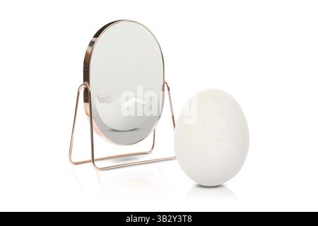 Oeuf entier réfléchissant dans le miroir comme fissuré, fond blanc. Opposé, contraste, différence Banque D'Images