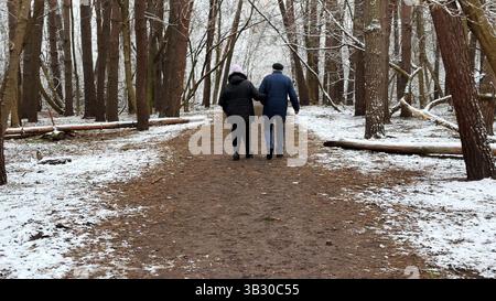 Couple mûr allant sur le chemin enneigé à la forêt de pins d'hiver. Mari senior et femme marchant à travers le sentier dans la forêt de conifères. Ancienne paire de Banque D'Images