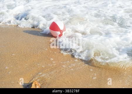 Ballon de plage rouge et blanc jouant avec les vagues et la mer à la plage Banque D'Images