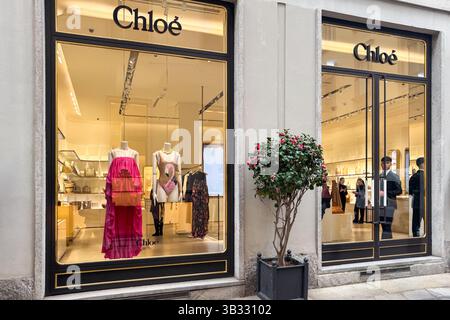 Milan, Italie - 12 avril 2025 : magasin Chloe à Milan. La fenêtre de la boutique est ornée d'une robe rose à volants et d'un maillot de bain. Intérieur et acheteurs élégants Banque D'Images