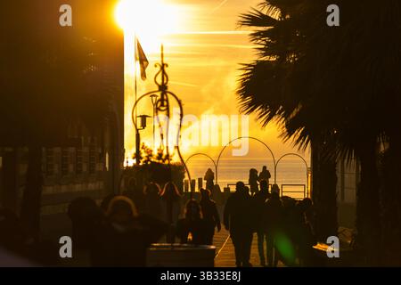 Sirmione, Italie - 01.2022 : coucher de soleil serein dans la scène urbaine côtière avec des gens silhouettés et des palmiers, lac de Garde Banque D'Images