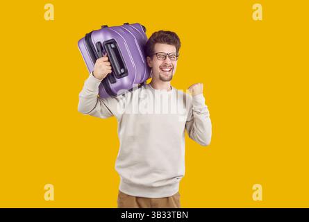 Homme avec valise violette sur l'épaule souriant montrant oui heureux de vacances sur fond jaune. Banque D'Images