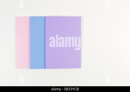 Vue de dessus des cahiers roses, violets et bleus sur fond blanc. École, papier peint de bureau. Pose à plat, espace de copie. Banque D'Images