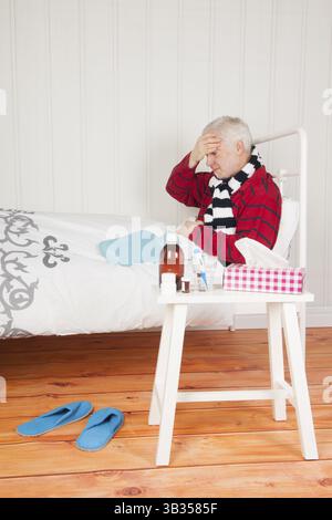 Homme malade senior avec mal de tête assis dans le lit avec des médicaments Banque D'Images