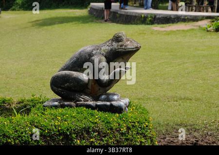 Statue en pierre d'une grenouille dans un parc sur un parterre de fleurs. Banque D'Images