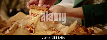 Gros plan des mains tirant une tranche de pizza pepperoni au fromage avec de délicieuses garnitures. Scène appétissante représentant du fromage fondu s'étirant d'une tranche de pizza Banque D'Images