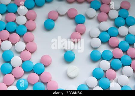 Des pilules blanches, bleues et roses en forme de point d'interrogation sont dispersées sur la table. Arrière-plan Banque D'Images
