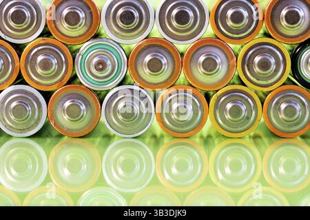 Plusieurs piles alcalines AA usagées sont vues disposées en pile sur une surface verte réfléchissante. Gros plan de face depuis le côté positif de la batterie Banque D'Images