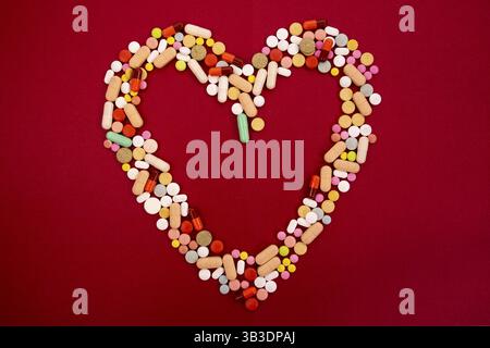 Colorés différents comprimés et capsules en forme de coeur vide sur un fond rouge. L'industrie pharmaceutique mondiale pour des milliards de dollars par année. Pharmace Banque D'Images