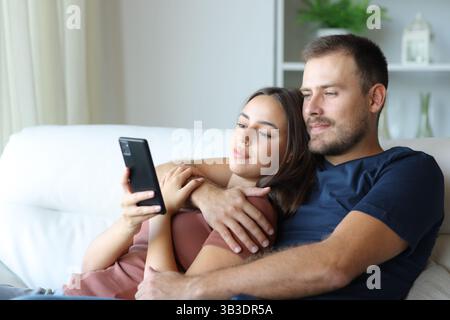 Couple détendu vérifiant le contenu du téléphone mobile assis sur un canapé à la maison Banque D'Images