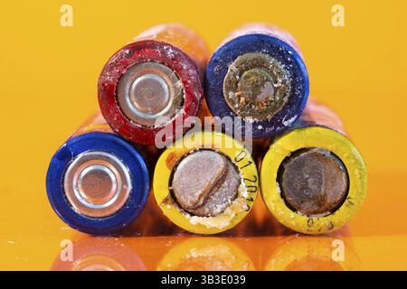Plusieurs piles alcalines AA défectueuses utilisées sont disposées dans un tas sur une surface orange réfléchissante. Gros plan sur la vue avant depuis le côté négatif de la batterie Banque D'Images