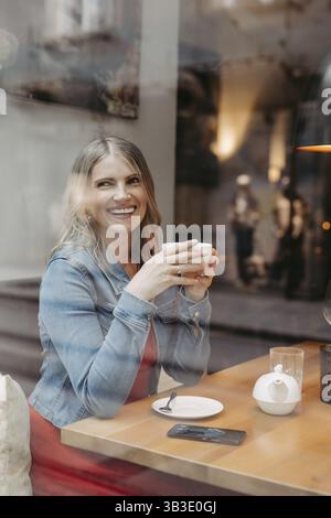 Blonde, femme séduisante, 40+, assise dans un café près de la fenêtre Banque D'Images
