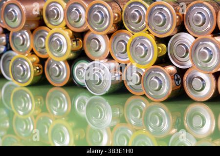 Plusieurs piles alcalines AA usagées sont vues disposées en pile sur une surface verte réfléchissante. Gros plan de face depuis le côté positif de la batterie Banque D'Images