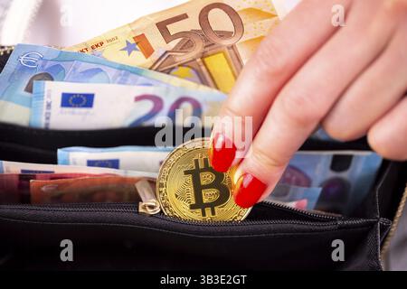 Crypto-monnaie virtuelle argent Bitcoin pièces d'or dans la main gauche d'une femme avec vernis à ongles rouge et un sac à main. L'avenir de l'argent. Billets en euros Banque D'Images