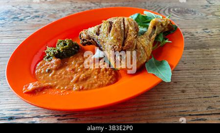 Poulet frit traditionnel indonésien mieux connu sous le nom de pecel ayam avec sauce Chili et légumes frais sur une table en bois Banque D'Images