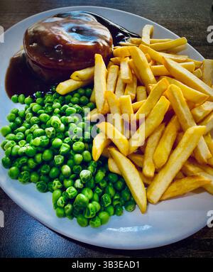 Un grand repas de café britannique classique composé de chips, pois, une tarte et une sauce sur une assiette ovale servie dans un café traditionnel du nord de Londres en Angleterre Banque D'Images