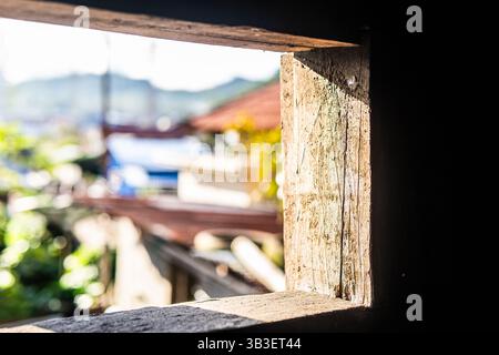 Lumière chaude du soleil passant à travers un cadre de fenêtre en bois rustique, avec une vue imprenable sur le village en arrière-plan. Banque D'Images