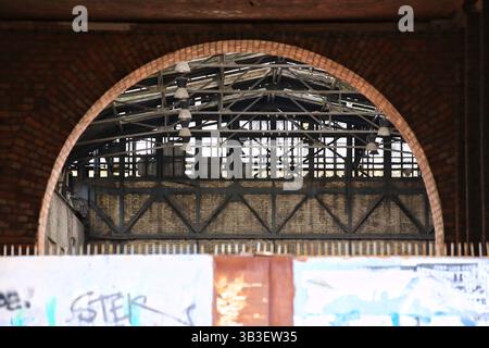 Arc en brique derrière la porte en acier encadrant un bâtiment industriel abandonné avec des poutres apparentes et des lampes suspendues. Banque D'Images