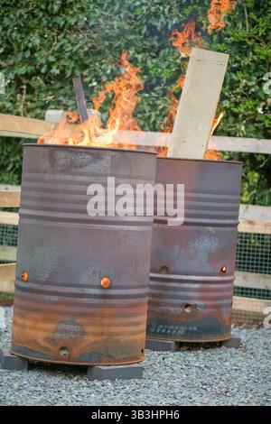 Brûler les déchets ménagers dans des barils d'huile en métal rouillé à l'extérieur, avec des flammes visibles et une clôture en bois en arrière-plan - installation de feu de joie de jardin rural britannique Banque D'Images