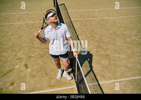 Un joueur confiant en vêtements de sport blancs se concentre sur le jeu tout en se tenant près du filet. Banque D'Images