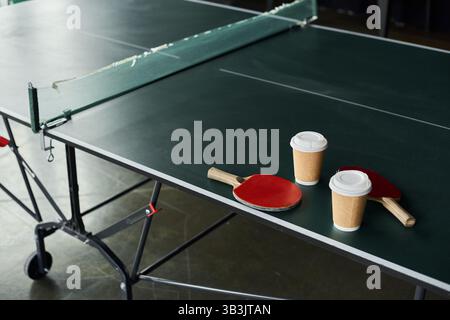 Deux palettes et tasses à café reposent sur une table à côté d'une table de ping-pong pendant une pause de travail. Banque D'Images