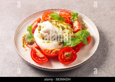 Salade caprese au fromage Burrata avec tomates cerises, huile d'olive, pesto et assaisonnement. Concept de nourriture fraîche. Banque D'Images
