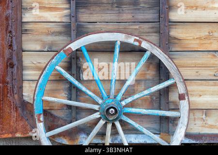 Une vieille roue de chariot à cheval devant un fond en bois. Gros plan sur les roues de wagon vintage Banque D'Images