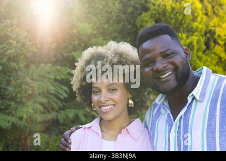 Couple souriant divers debout dans un jardin verdoyant luxuriant, avec le feuillage filtrant la lumière du soleil Banque D'Images