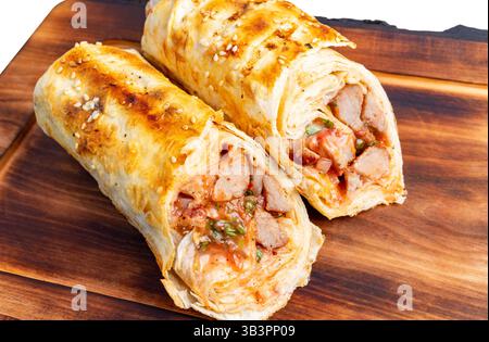 Deux wraps fraîchement grillés reposent sur une planche de bois, révélant une garniture de viande, de légumes et de sauce. La croûte dorée est parfaitement grillée, créant un Banque D'Images