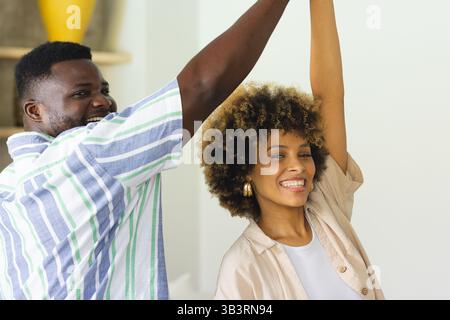 Couple dansant divers se tenant par la main tout en tournant dans le salon, avec vase jaune sur l'étagère Banque D'Images