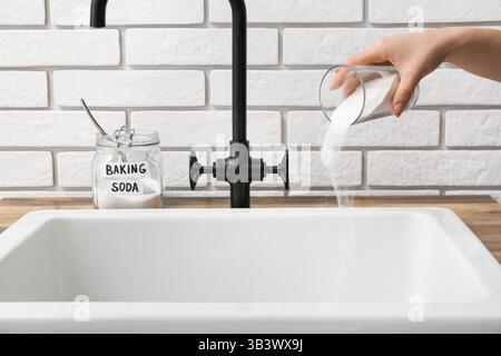 Femme versant du bicarbonate de soude dans un évier bouché, gros plan Banque D'Images