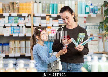 Une femme scanne un ensemble de brosses à dents dans une pharmacie à côté de son enfant Banque D'Images