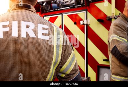 Équipe de pompiers - pompiers équipés de l'uniforme de l'équipe de pompiers d'intervention des services d'urgence et de l'équipement près du moteur de pompiers rouge du service. camion. Banque D'Images