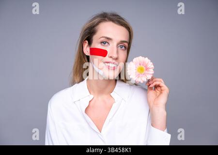 Femme avec des bandes kinesio sur son visage dans un tournage en studio. Concept de réhabilitation musculaire faciale, cosmétologie et soins de la peau. Léger, style médical. Banque D'Images