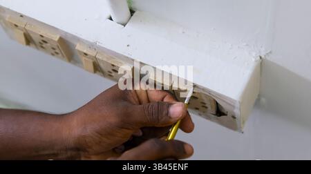 Personne installant des prises électriques sur un mur blanc avec un outil pour des réglages précis lors de la rénovation. Banque D'Images