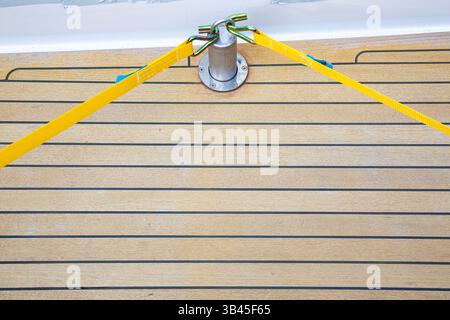 Deux sangles de cargaison en jaune sont fixées et tendues sur une jambe de force, qui est boulonnée au pont en teck du yacht. Banque D'Images