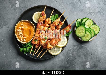 Satay de poulet grillé avec sauce aux cacahuètes épicée sur table en béton foncé, vue de dessus, espace de copie. Sate ayam. Repas en brochettes thaïlandaises de style asiatique. Banque D'Images