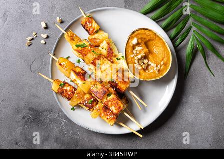Brochettes satay de tofu grillé et d'ananas avec sauce aux arachides épicée sur fond de béton gris, vue de dessus. Kebabs frits au fromage halloumi. Végétalien végétarien Banque D'Images
