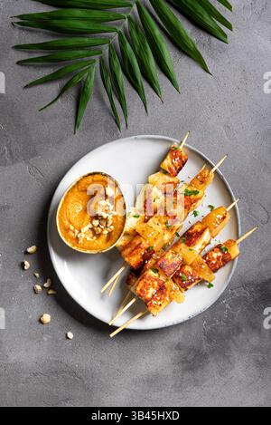 Brochettes satay de tofu grillées et d'ananas et sauce épicée aux cacahuètes sur fond de béton gris, vue de dessus. Cuisine thaïlandaise végétarienne asiatique. Banque D'Images