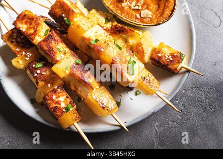 Brochettes satay de tofu grillées et d'ananas avec sauce aux cacahuètes épicée de près. Kebabs frits au fromage halloumi. Nourriture végétarienne végétalienne. Banque D'Images
