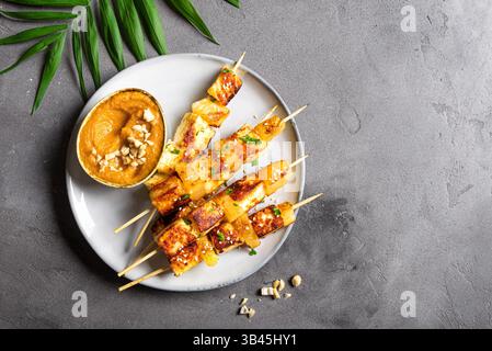 Brochettes satay de tofu grillé et d'ananas et sauce épicée aux cacahuètes sur fond de béton gris, vue de dessus, espace copie. Végétalien asiatique végétarien style thaïlandais f Banque D'Images